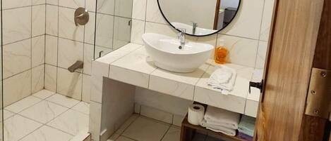 Een badkamer met een douche, wastafel en spiegel.