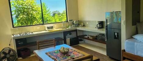 Cocina compacta con ventana, una mesa con mantel individual y un refrigerador.