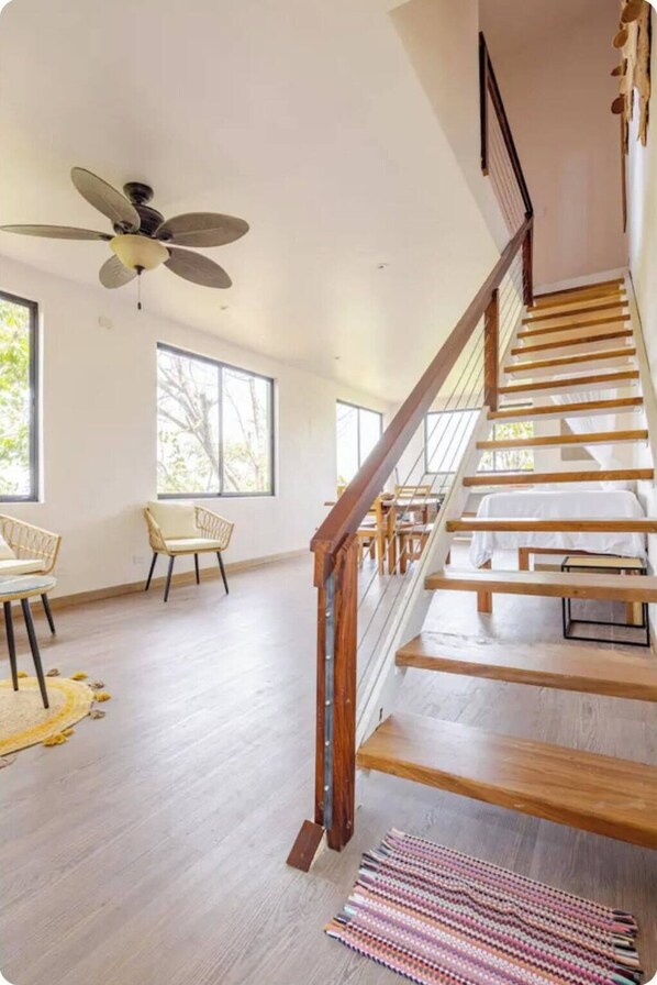 Une pièce spacieuse avec un escalier en bois, un ventilateur de plafond et de grandes fenêtres.
