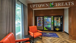 Un vestíbulo de hotel con una zona de estar, una máquina expendedora etiquetada 'UPTOWN TREATS' y una máquina 'Food Court Express'.