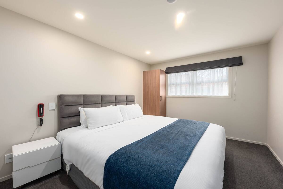 A bedroom with a bed, a nightstand, a wardrobe, and a window with blinds.