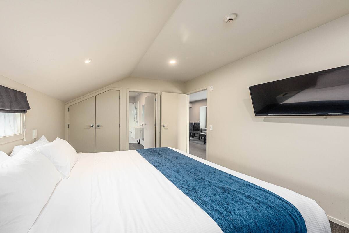 A bedroom with a bed, a TV, a wardrobe, and a bathroom visible through an open door.