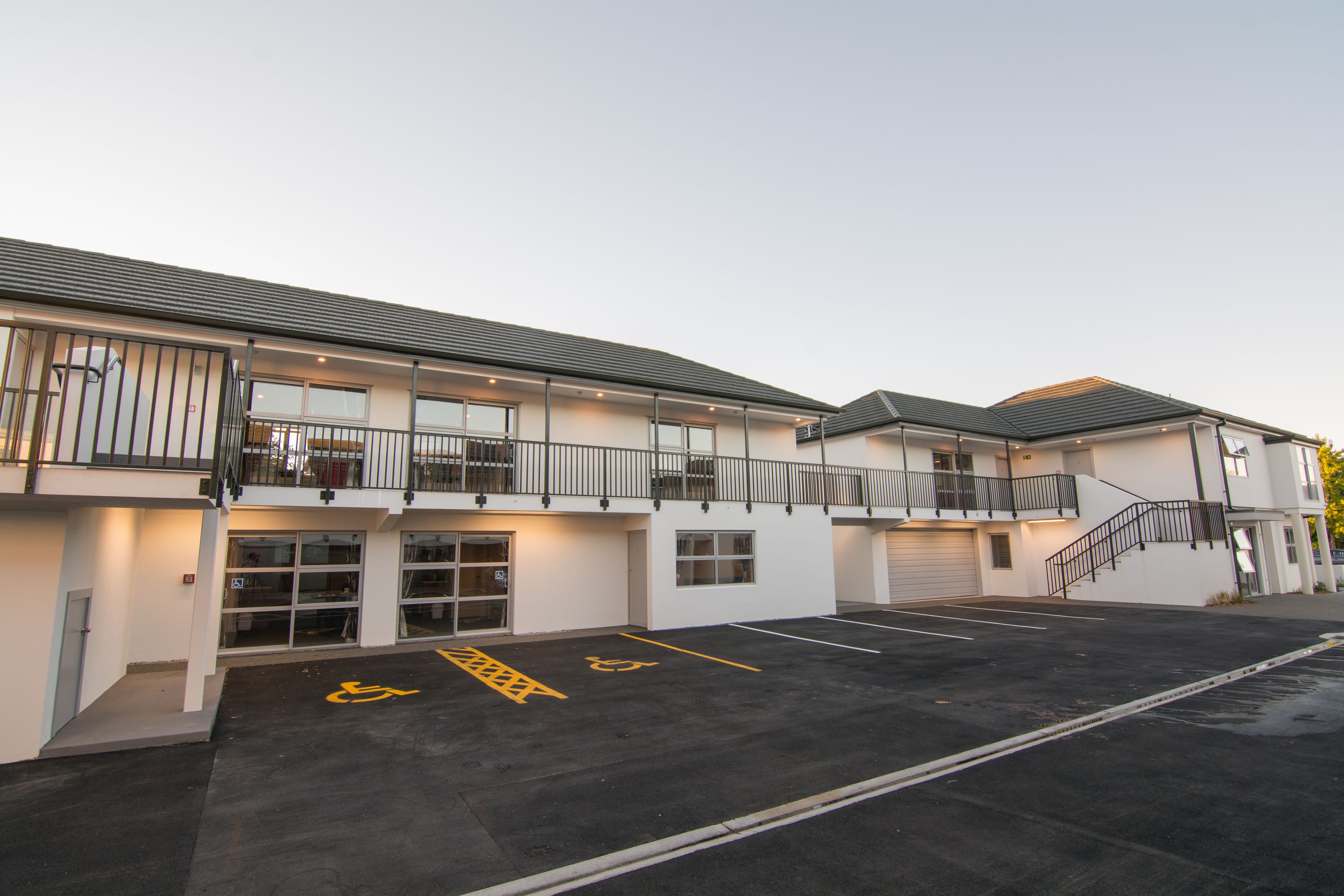 A modern building with a parking lot, marked handicapped spaces, and a staircase leading to a second floor.
