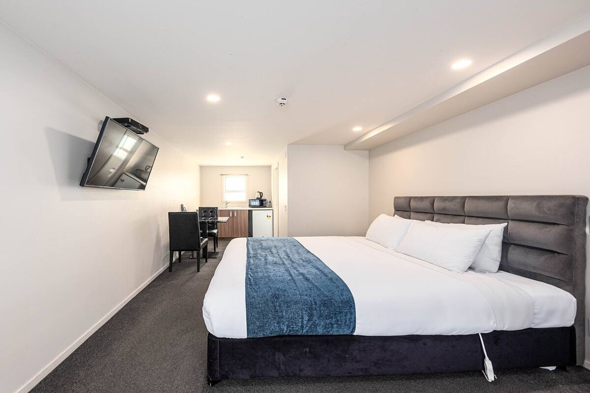 A hotel room with a large bed, a desk, and a kitchenette.