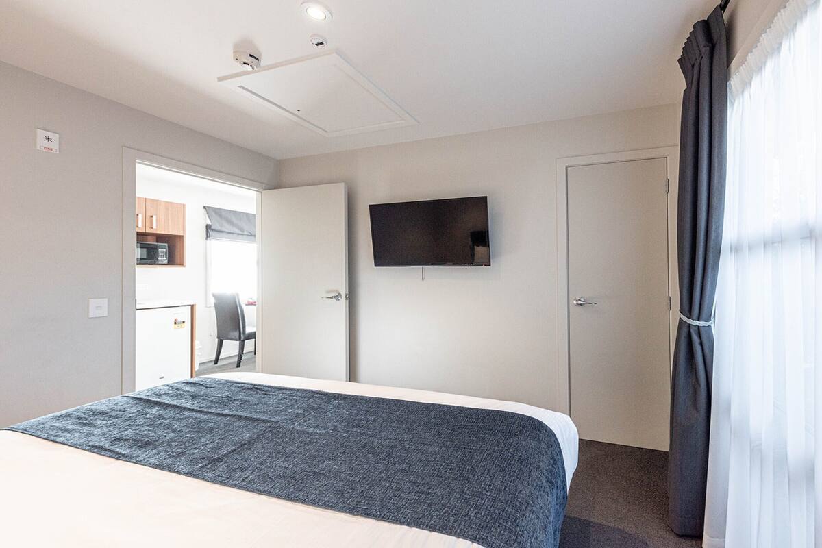 A hotel room with a bed, a flat-screen TV mounted on the wall, a door, and a window with curtains.