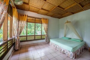Una habitación con una cama, una ventana con cortinas, un ventilador y una mosquitera.