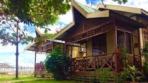 A traditional wooden building with a sloped roof and lattice windows, surrounded by greenery and a stone pathway.
