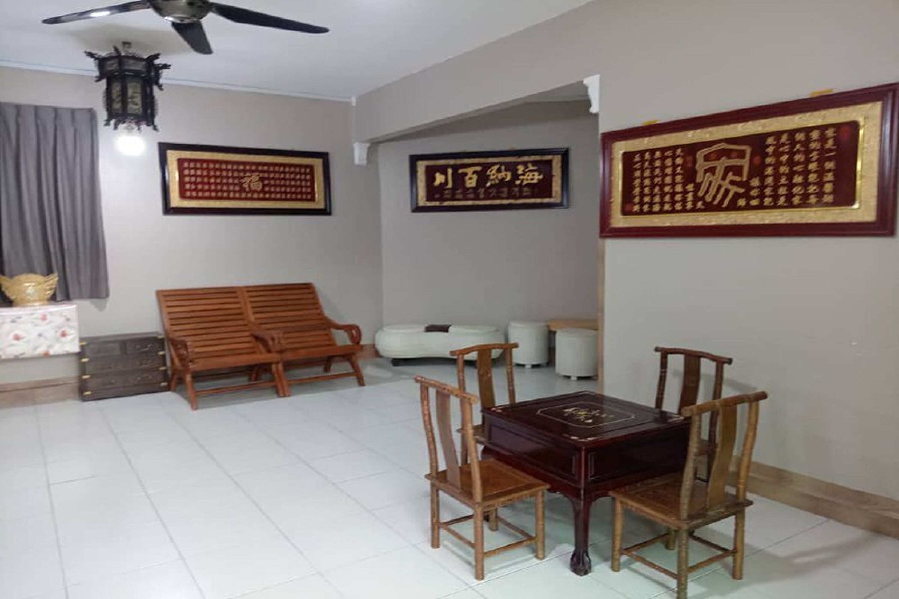 A room with a ceiling fan, a sofa, a dining table with chairs, and framed calligraphy art on the walls.