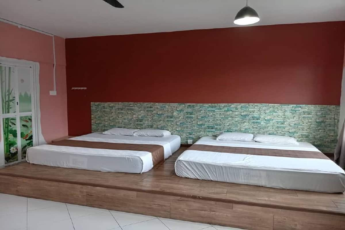 A room with three beds, a tiled floor, a red wall, and a textured wall behind the beds.