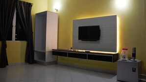 A room with a flat-screen TV mounted on a wall, a built-in shelf below, and a small refrigerator on the right. - Aeon Tebrau Apartment Johor Bahru (Johor Bahru)