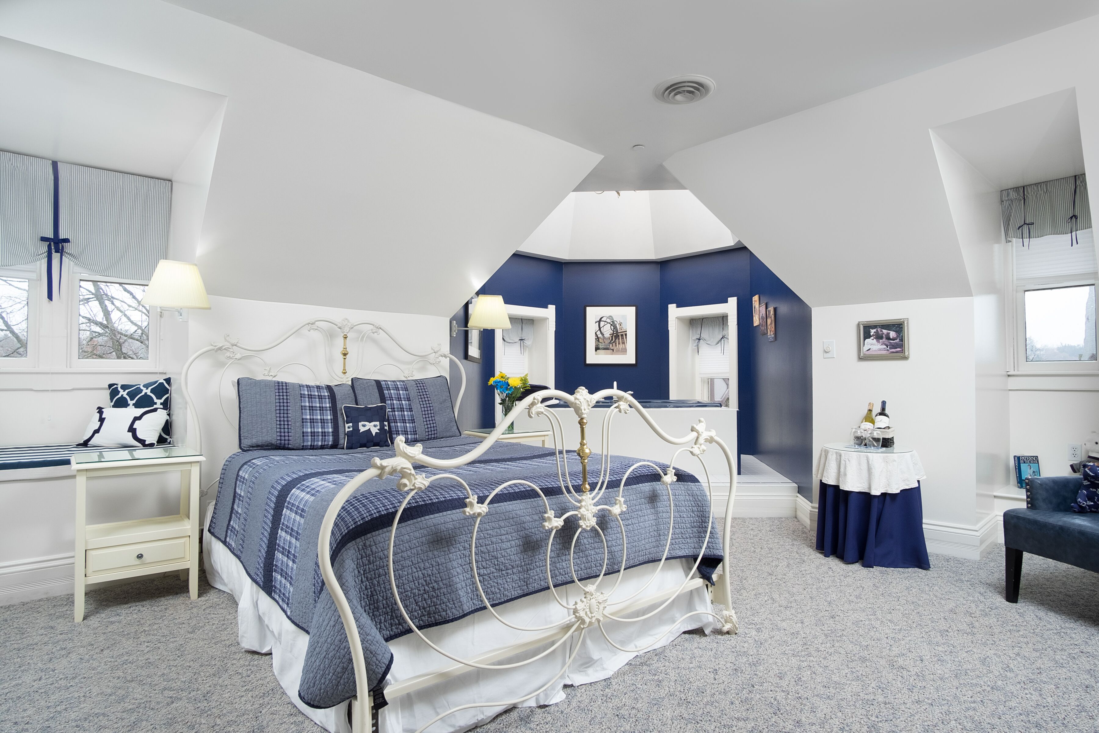 A bedroom with a bed, a nightstand, a dresser, a window, and a small table with a lamp.