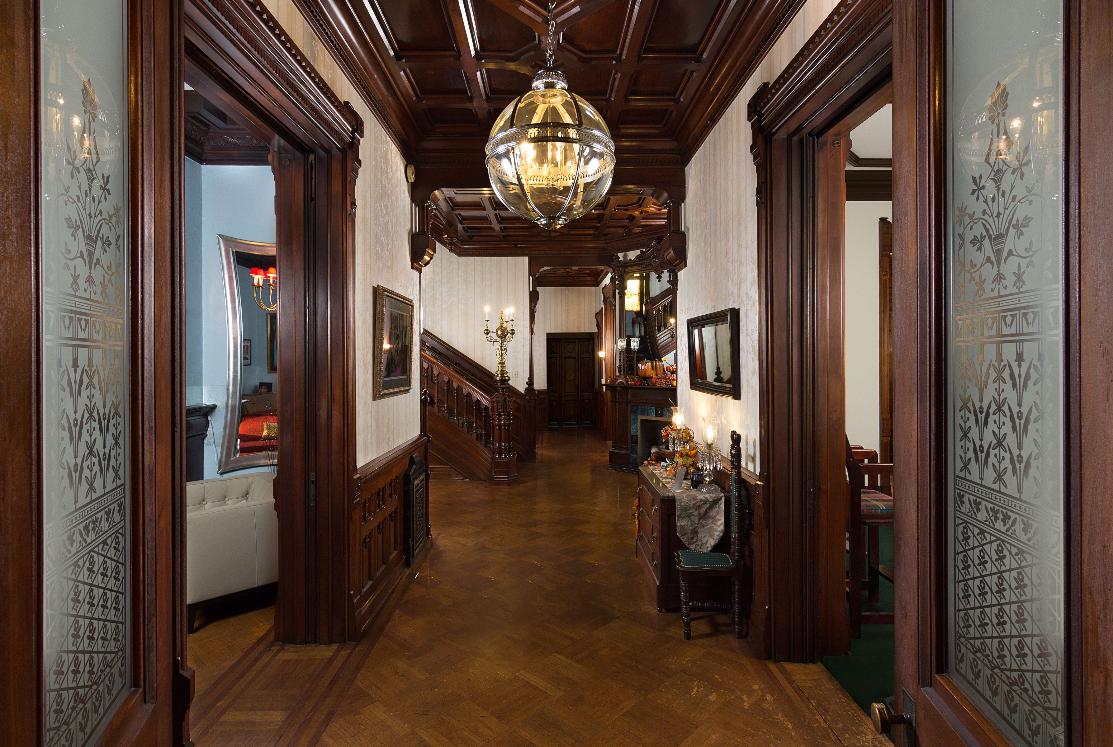 A grand hallway with wooden paneling, a chandelier, and a staircase leading to another level.