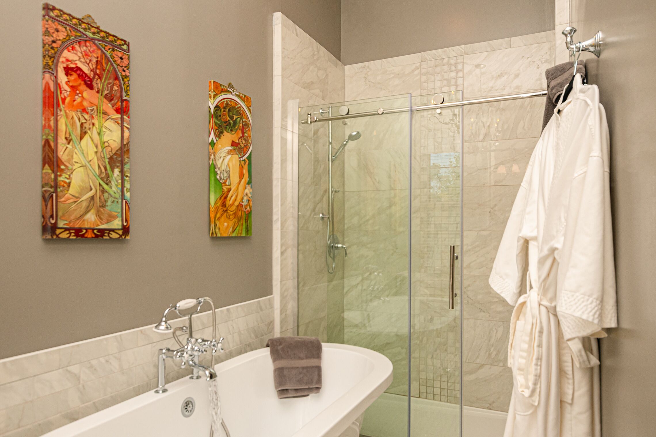 A bathroom with a glass-enclosed shower, a white bathtub, and two wall-mounted paintings.