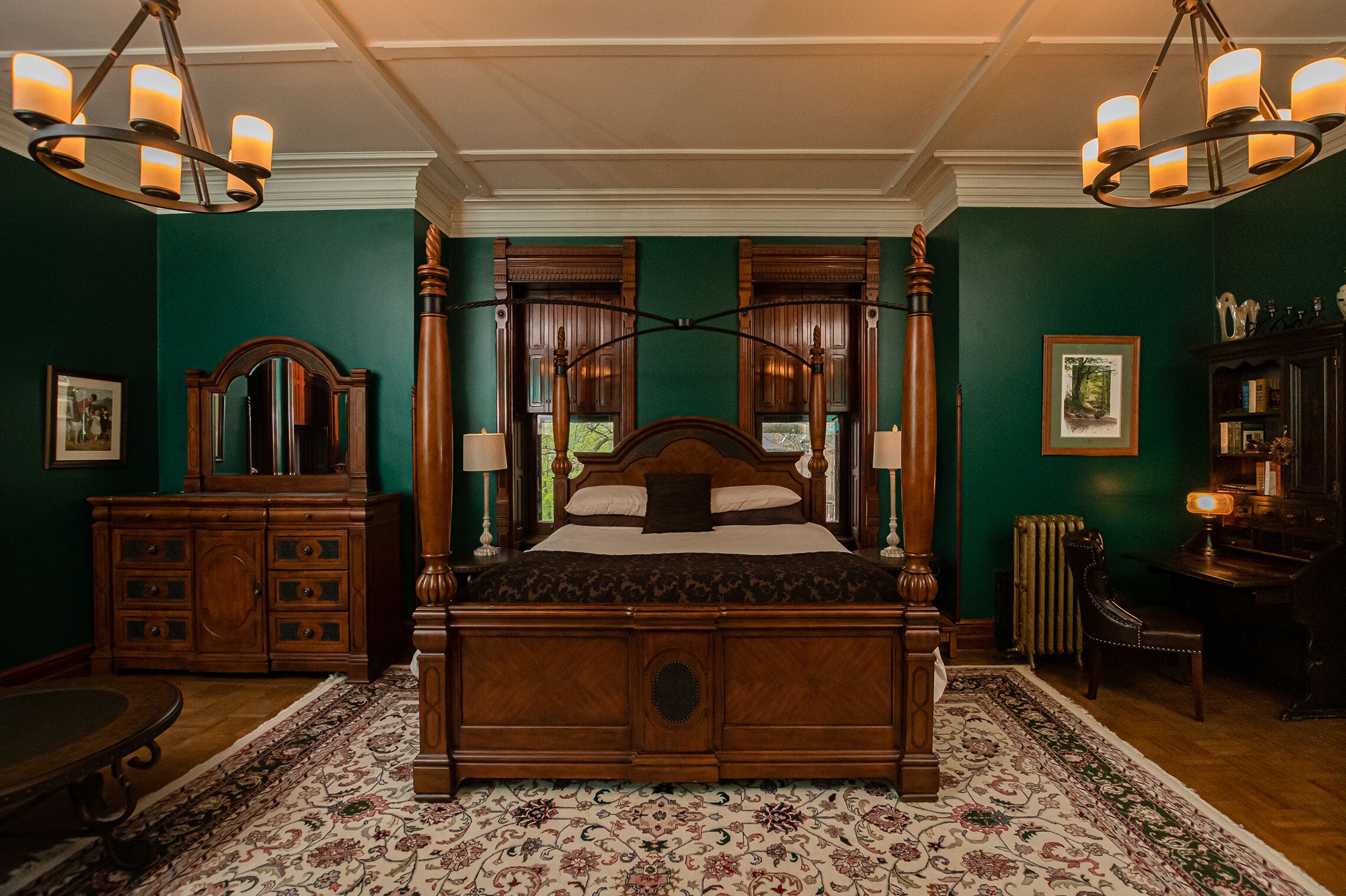 A traditional bedroom with a four-poster bed, wooden furniture, and a green wall.
