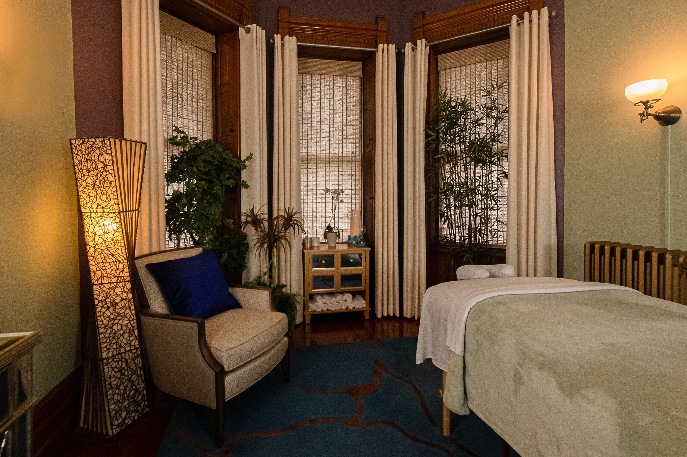 Une chambre d’hôtel avec un lit, une chaise, une lampe sur pied et une petite table sur laquelle est posée une plante.