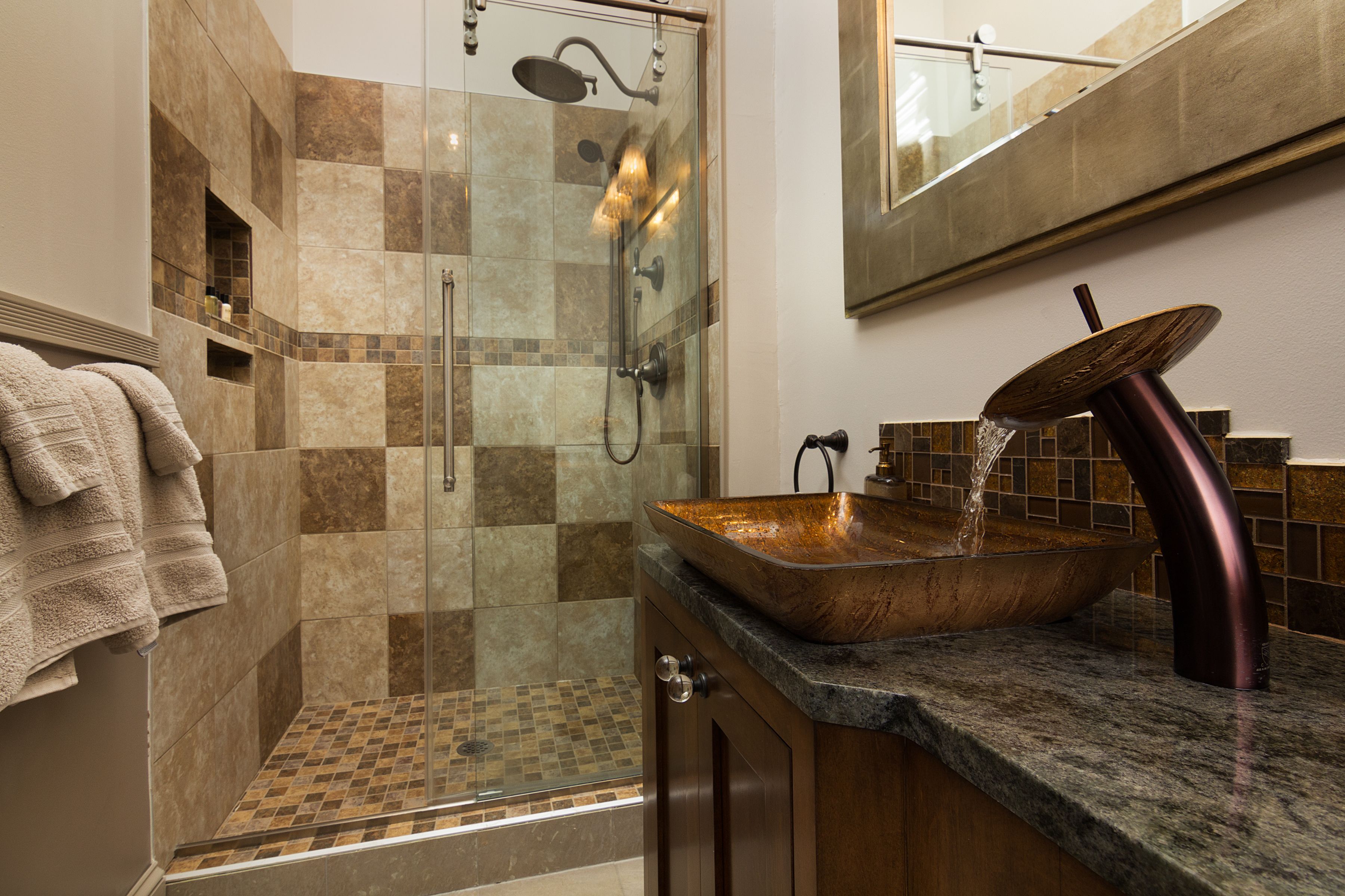 A modern bathroom with a glass-enclosed shower, a copper sink, and a large mirror.