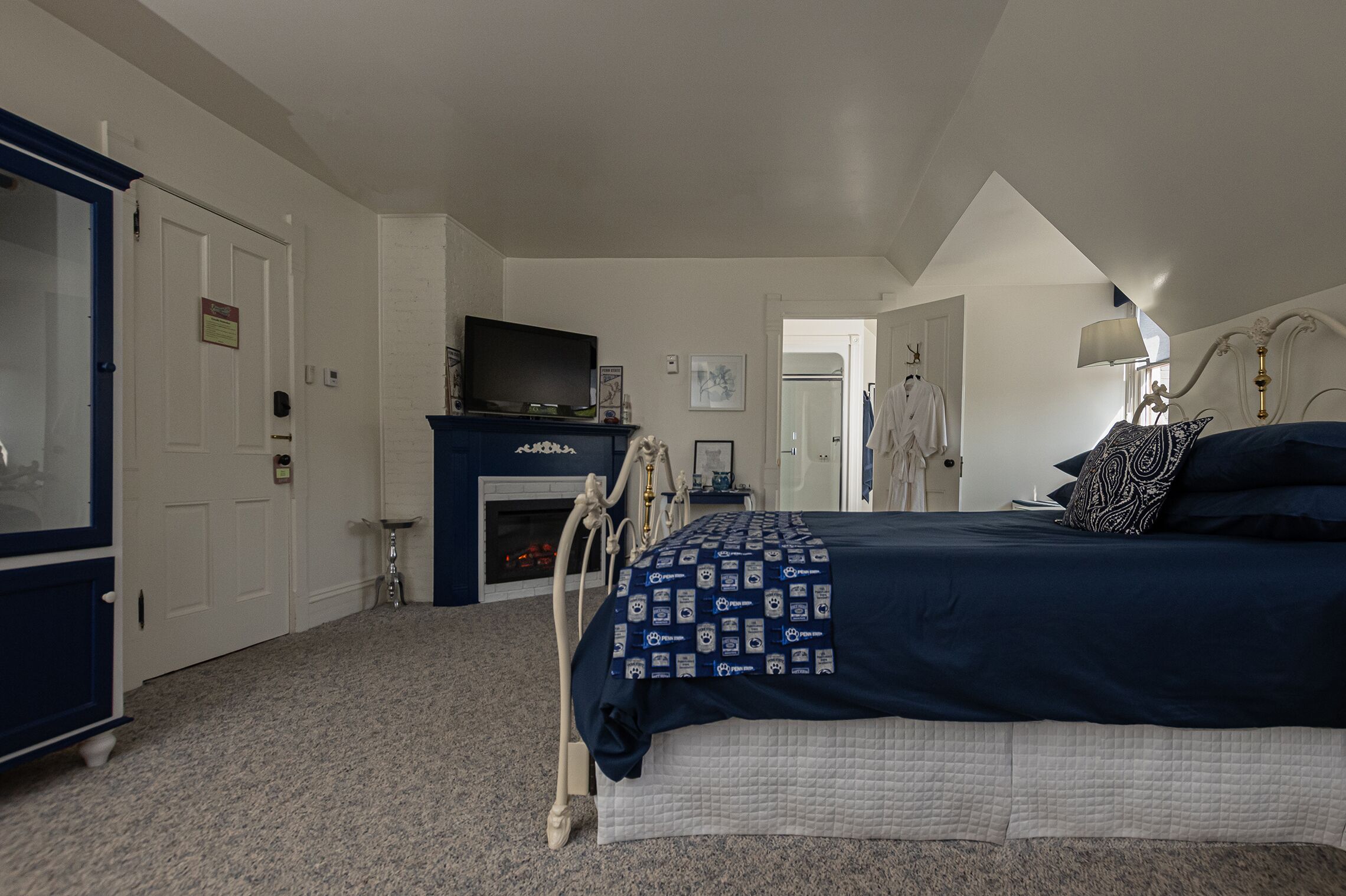 A bedroom with a large bed, a fireplace, a television, and a wardrobe.