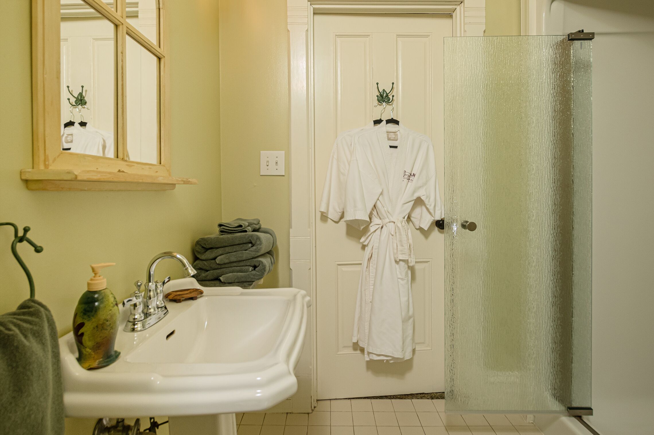 A bathroom with a sink, mirror, and two white robes hanging on a door.