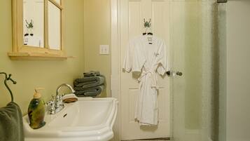 A bathroom with a sink, mirror, and two white robes hanging on a door.