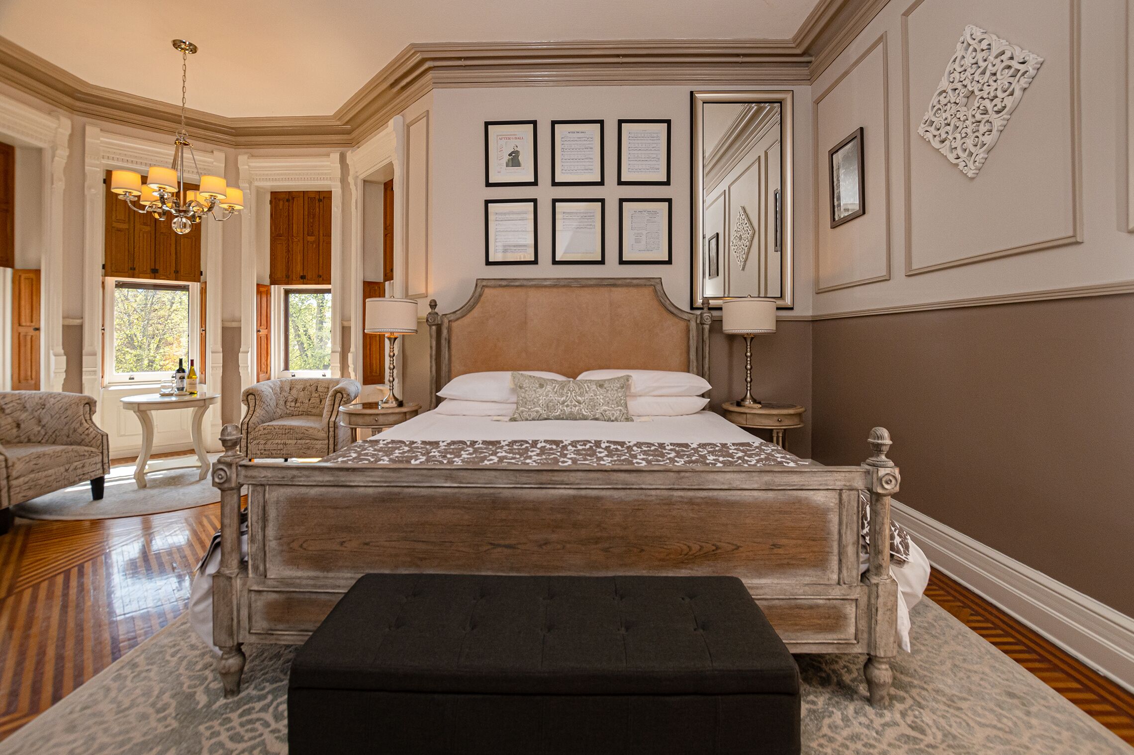 A spacious bedroom with a large bed, two bedside tables, a chandelier, and a view of the outdoors.