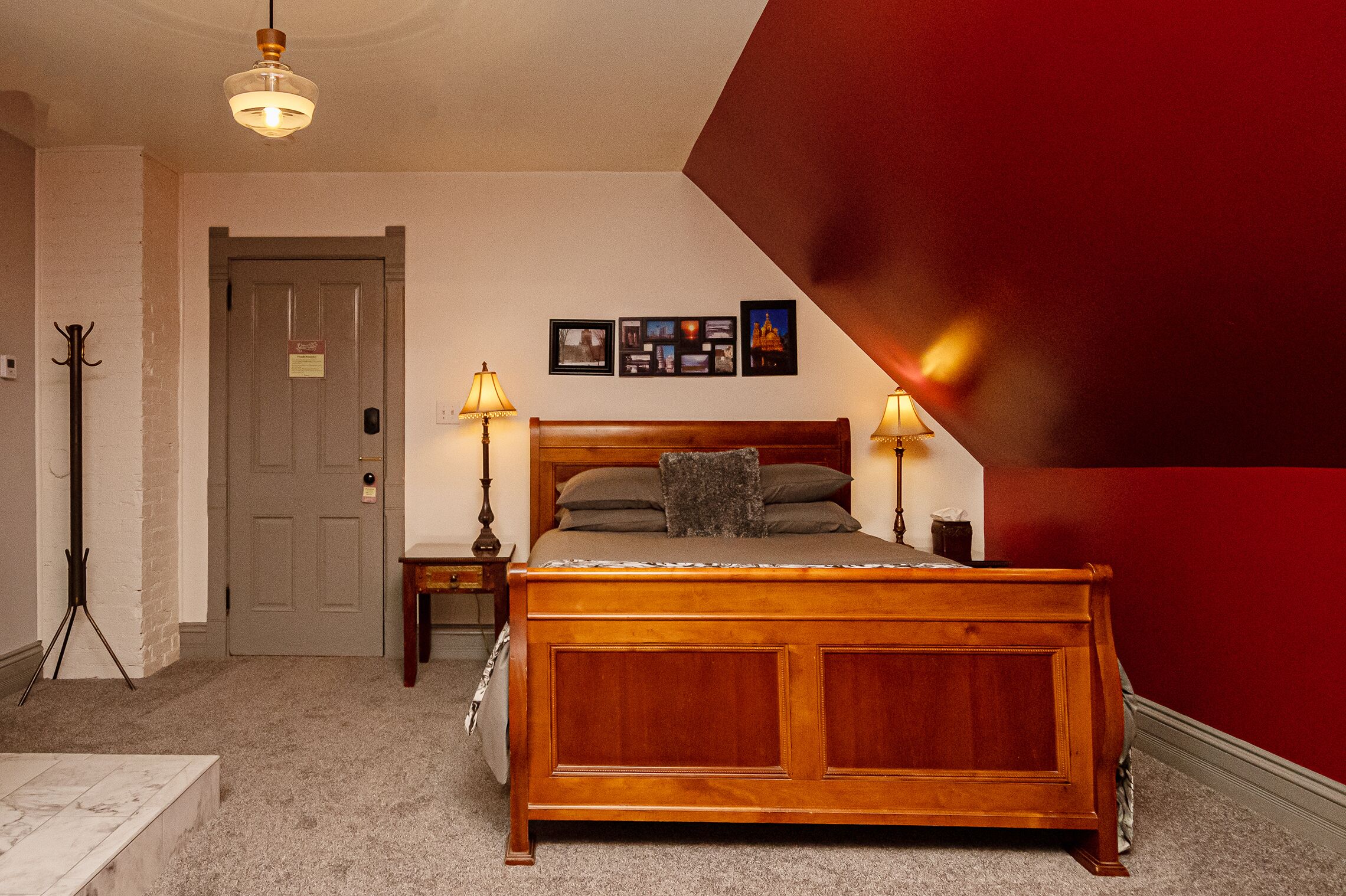 A bedroom with a wooden bed, two bedside lamps, a door, and a wall with framed pictures.