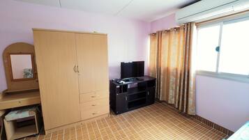 A room with a wardrobe, a television on a stand, a window with curtains, and a tiled floor.
