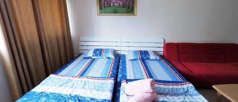 A room with two beds, a red sofa, a wooden curtain, and a framed picture on the wall.