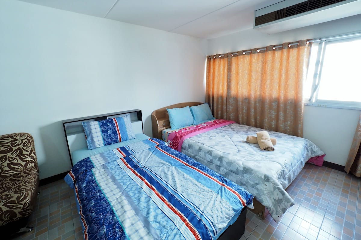 Ein Zimmer mit zwei Betten, einem gemusterten Sessel und einem Fenster mit Vorhängen.