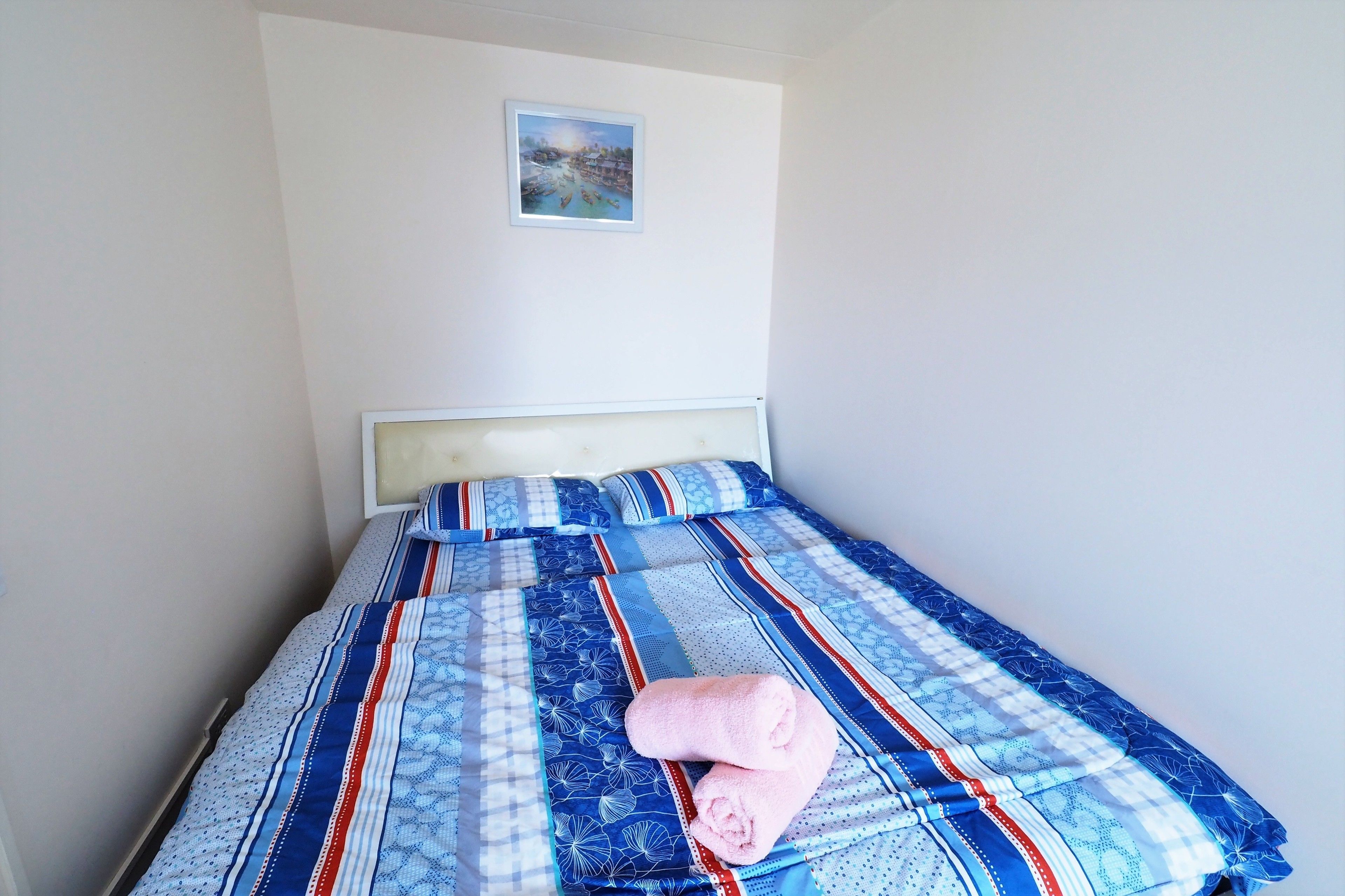 A neatly made bed with a blue and white patterned bedspread and pillows, a framed picture on the wall, and a white headboard.