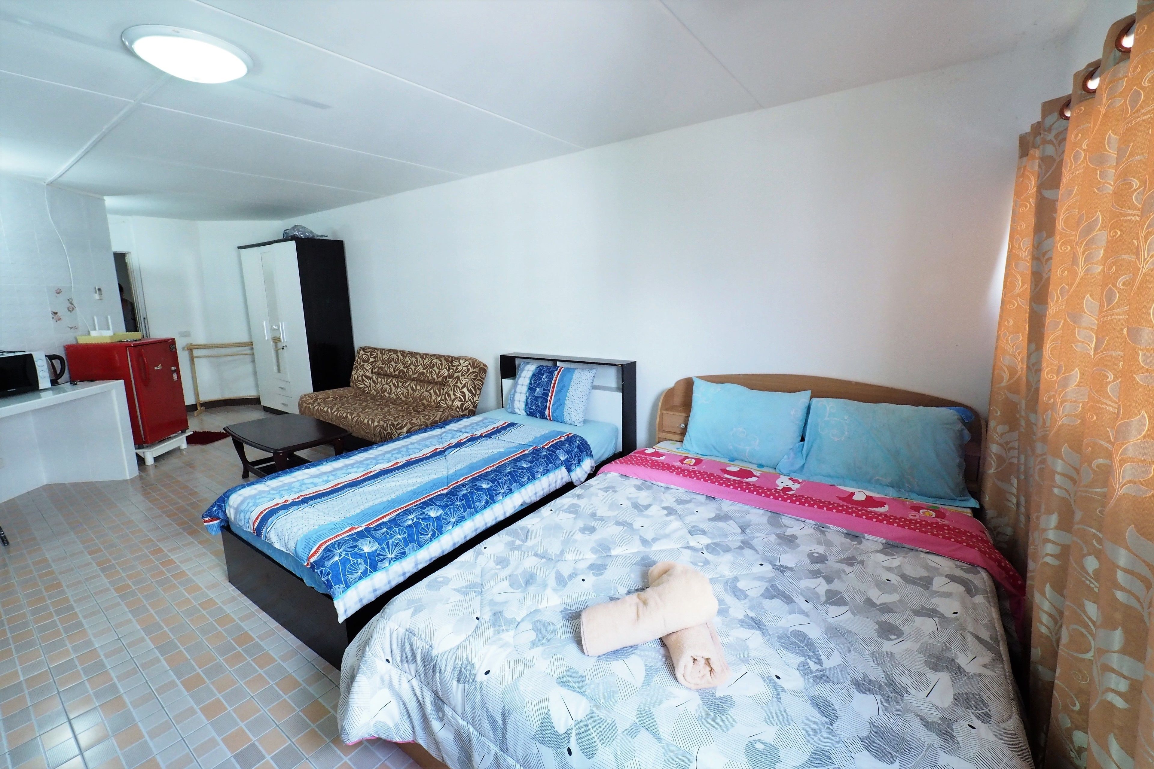 A hotel room with two beds, a desk, a wardrobe, and a patterned curtain.