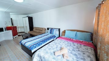 A hotel room with two beds, a desk, a wardrobe, and a patterned curtain.