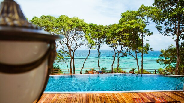 Una terraza de madera con piscina, rodeada de árboles y con vistas al mar.