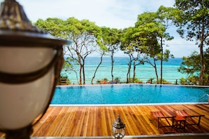 Una terraza de madera con piscina, rodeada de árboles y con vistas al mar.