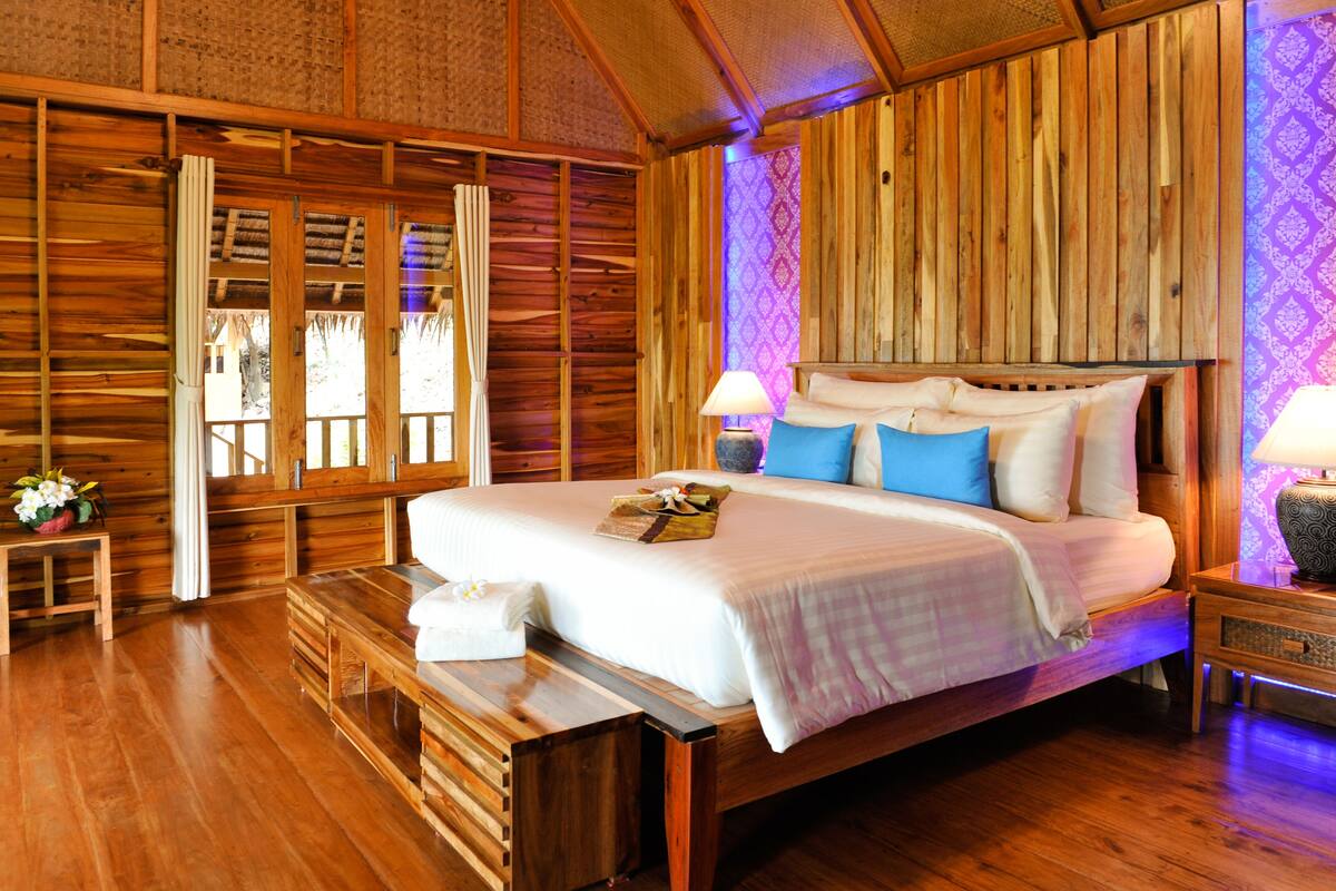 Un dormitorio tipo cabaña de madera con una cama grande, paredes de madera y una ventana con cortinas.