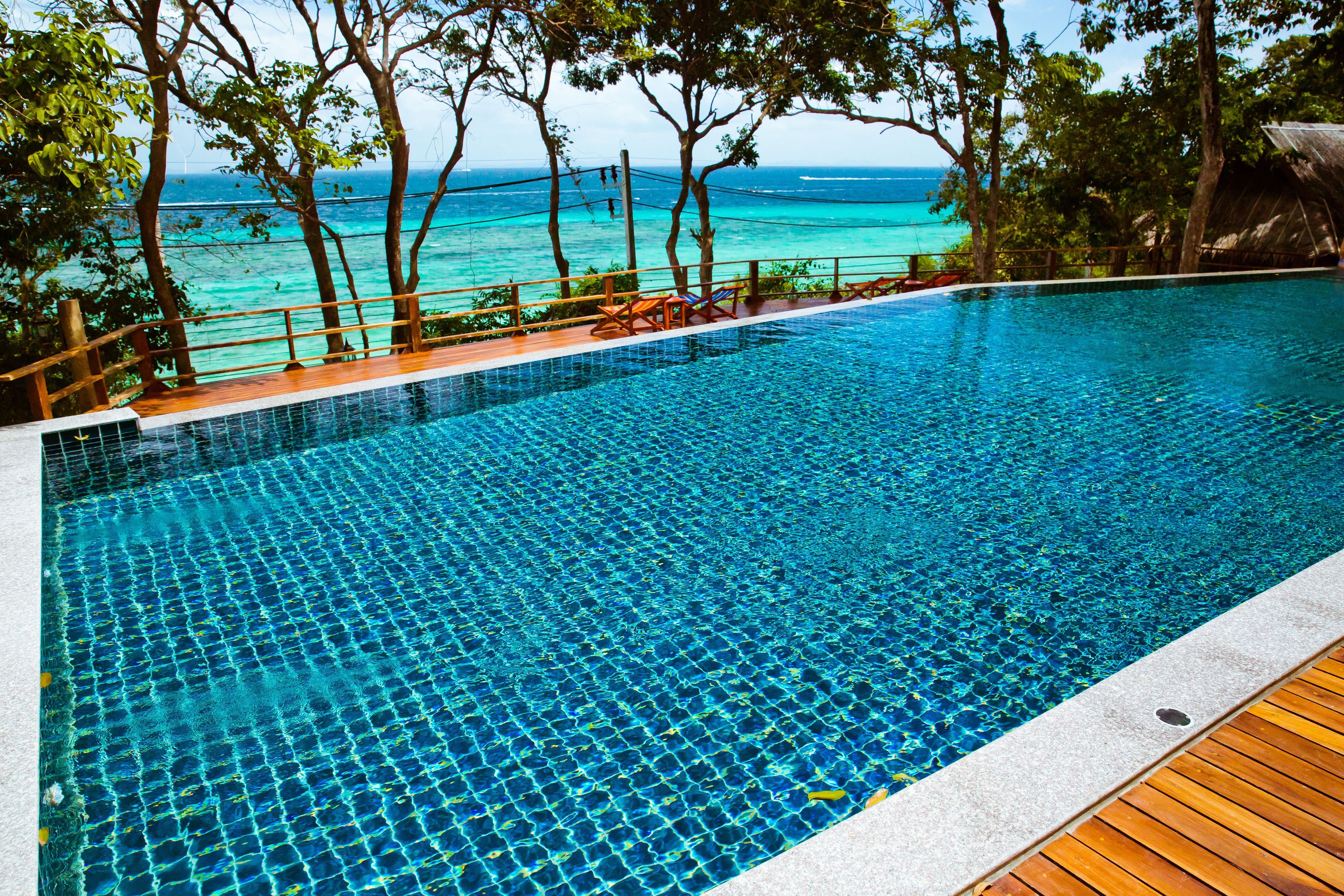 Una piscina azul cristalina con una cubierta de madera y vistas al océano.