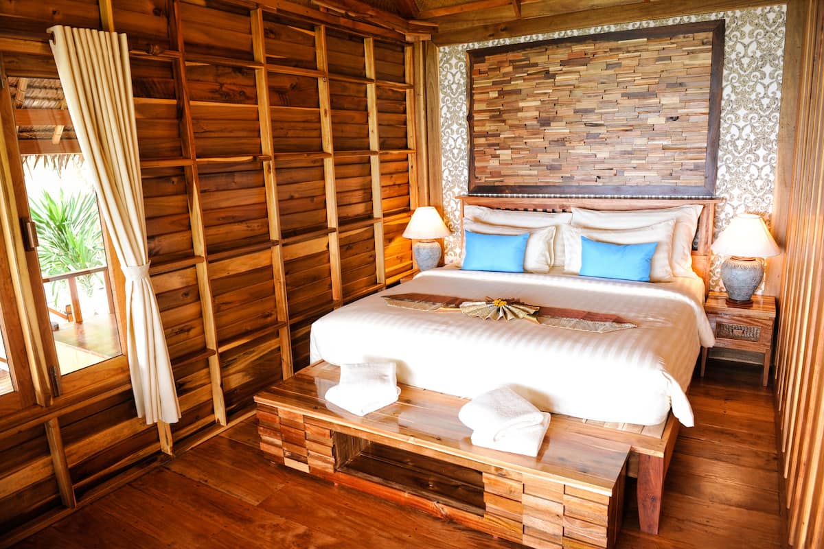 Una habitación de madera con una cama, dos mesitas de noche y una ventana con cortinas.