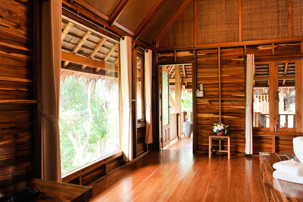 Interior de madera con ventanas amplias, un banco de madera y una pequeña mesa con un florero.