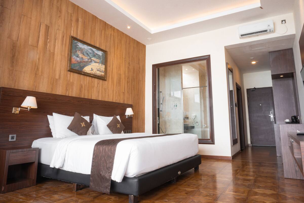 Ein Hotelzimmer mit einem großen Bett, Holzwandverkleidung, einem Gemälde, einem Fernseher und einem Badezimmer mit Glastür.
