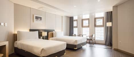 Une chambre d’hôtel avec deux lits, une petite table, une chaise et une fenêtre donnant sur des immeubles.
