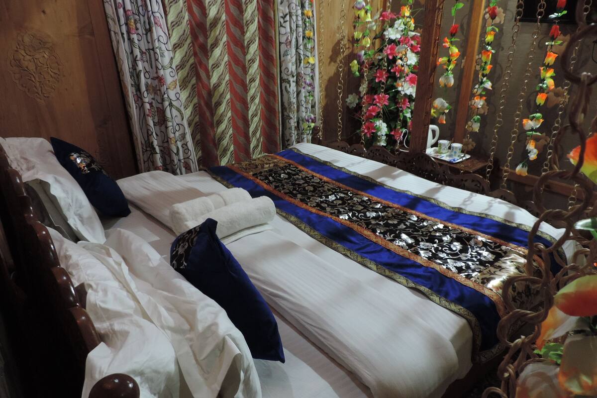 A neatly made bed with white linens and blue pillows, a decorative bedspread, and a floral curtain.