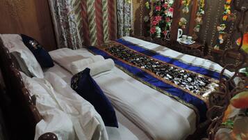 A neatly made bed with white linens and blue pillows, a decorative bedspread, and a floral curtain.