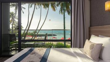 A hotel room with a large bed, a view of the ocean, and a balcony with red umbrellas.