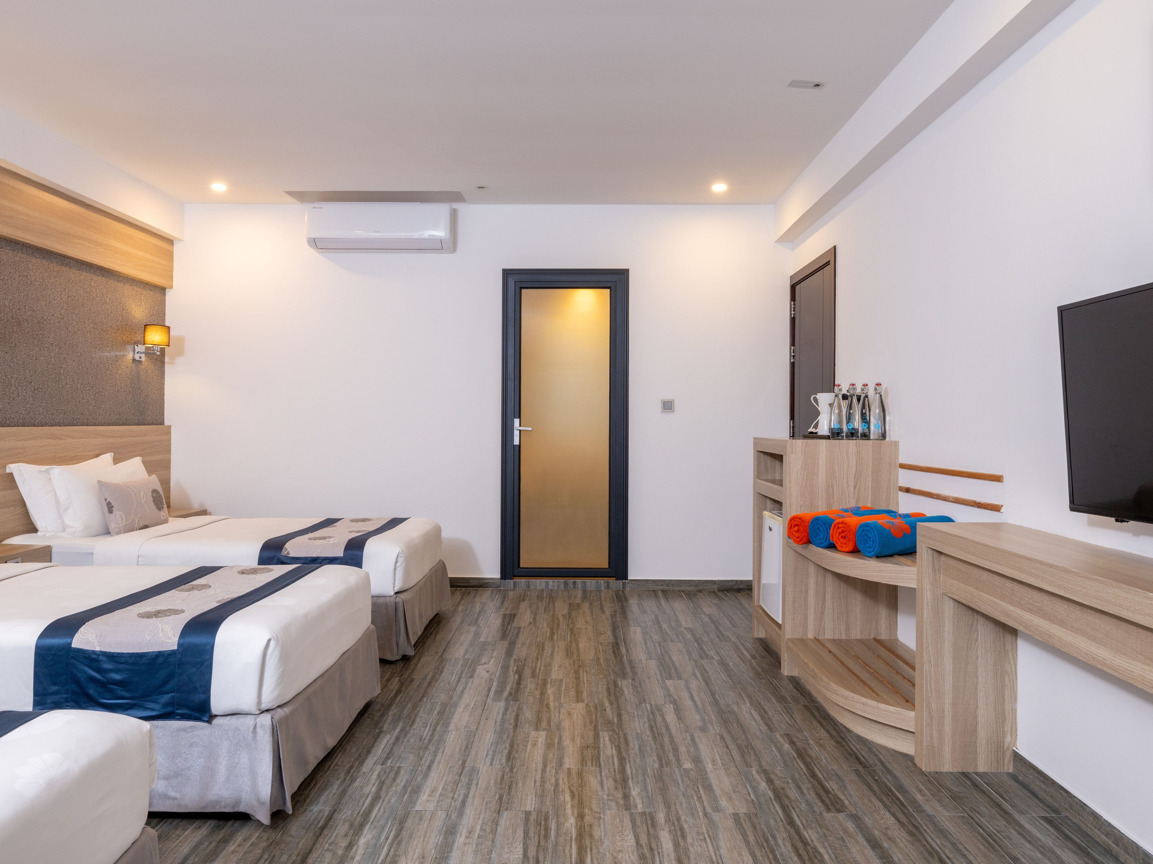 A hotel room with two beds, a desk with a TV, a mirror, and a door.
