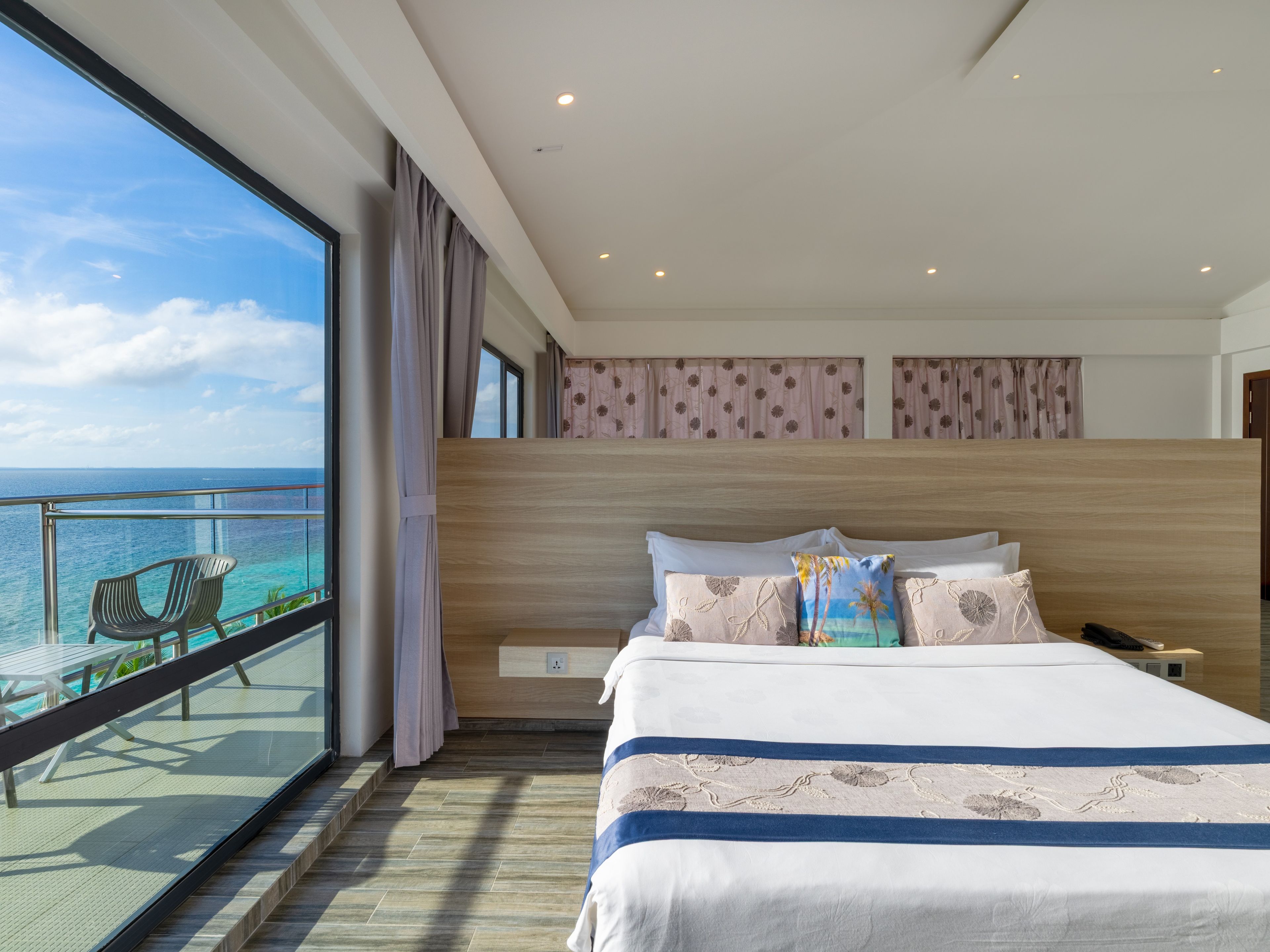 Habitación de hotel con una cama grande, vistas al océano y un balcón con sillas.