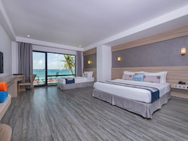 Quarto de hotel com uma cama grande, uma cama menor, uma escrivaninha e vista para o oceano.