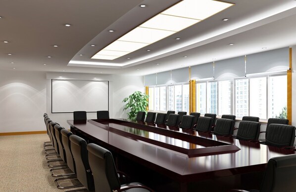 Un salón de conferencias con una larga mesa, sillas, una pantalla de proyector y ventanas amplias con cortinas.