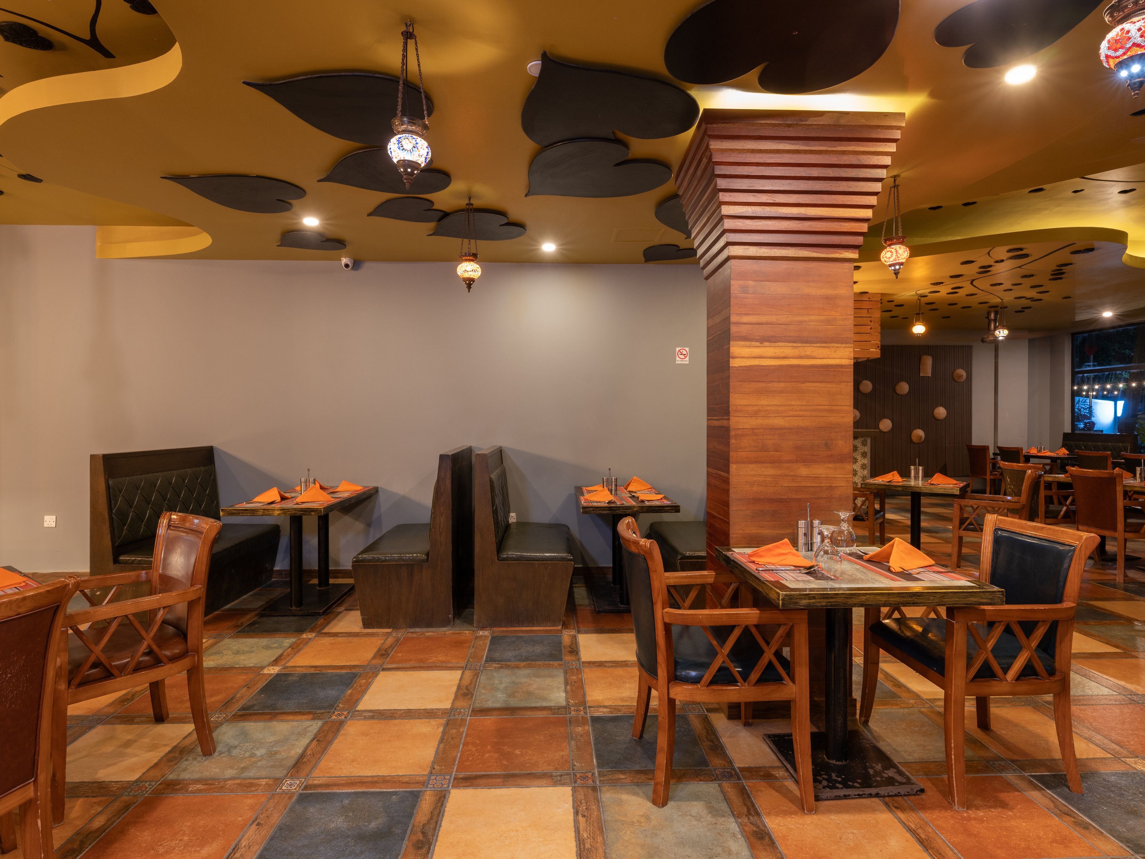A restaurant interior with wooden furniture, tiled flooring, and decorative ceiling elements.