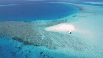Luchtbeeld van een strand met helder turquoise water, een zandrijk eiland en een klein bootje.