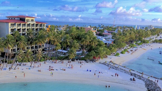 A beach resort with a large building, palm trees, and a sandy beach. - Kaani Grand Seaview (Maafushi)