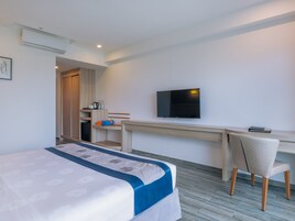 Habitación de hotel con cama, escritorio, silla, televisión y kitchenette.